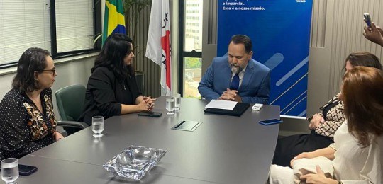 Desembargador Ramom Tácio sentado à cabeceira de uma mesa. Há quatro mulheres sentadas na mesa. ...