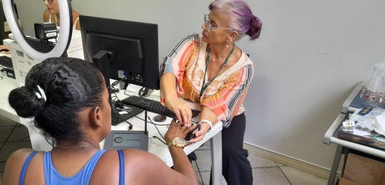 Foto mostra uma servidora colhendo as digitais de uma eleitora.