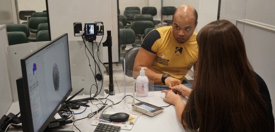 Rapaz observa uma mulher assinando em equipamento digital, assinatura aparece na tela do computa...