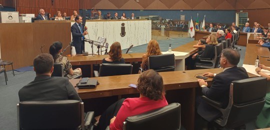 Desembargador Ramom Tácio de pé durante discurso. Algumas pessoas sentadas observam.