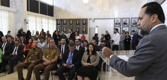 Desembargador Ramom Tácio, no canto direito. Ao fundo, homens e mulheres na plateia observam.