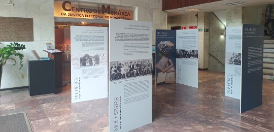 Foto mostra biombos com textos e fotos em frente à entrada do Centro de Memória do TRE-MG.