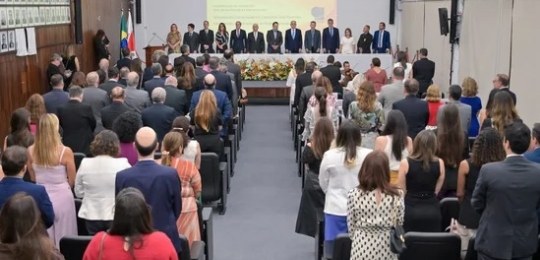 Foto mostra um auditório cheio, com pessoas de pé na plateia e sobre o palco.