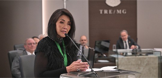 Noriko Tsukamoto durante discurso. Ao fundo, integrantes da Corte Eleitoral.