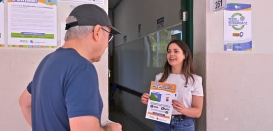 Foto de mesária mostrando cartaz do referendo de BH a um eleitor