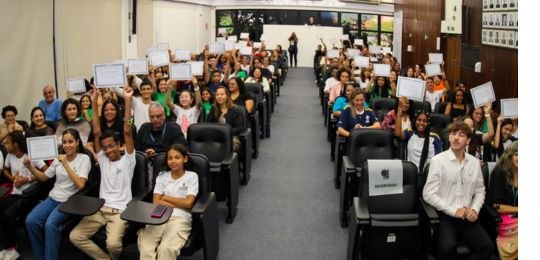 foto de um auditório com vereadores mirins eleitos mostrando seus diplomas