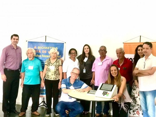 Foto com servidores e pessoas com mais de 70 anos em torno de uma mesa